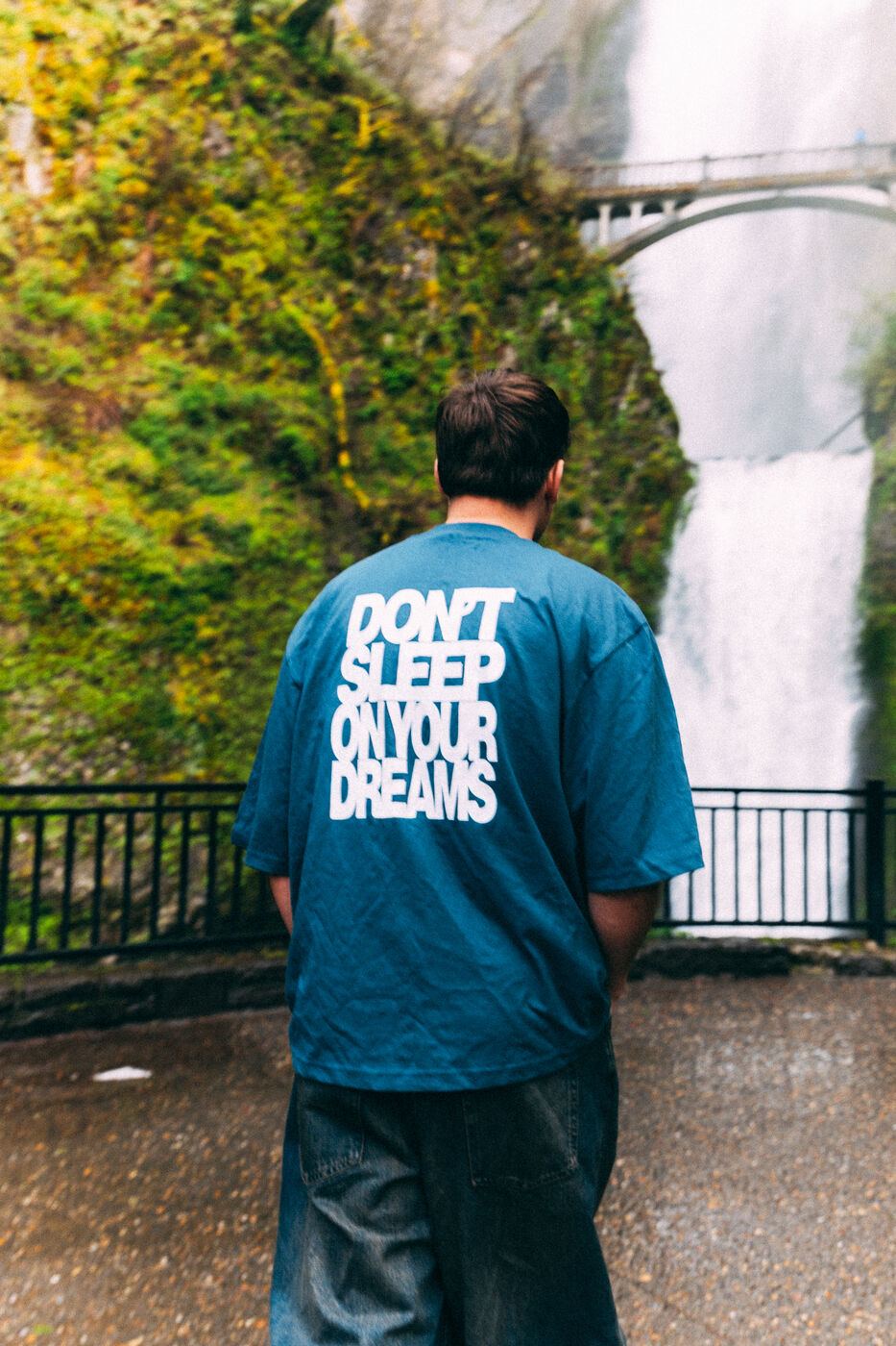 A Don't Sleep On Your Dreams tee in front of a waterfall